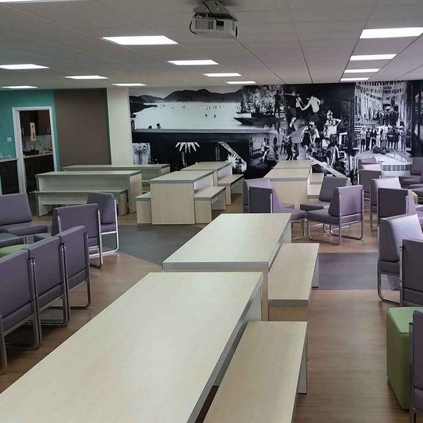 Empty modern cafeteria with white tables, purple chairs, and a black-and-white wall mural