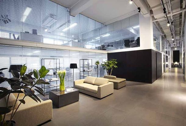 Modern office lounge with beige sofas, potted plants, and glass walls under bright industrial lighting
