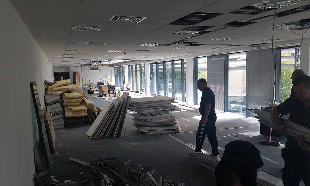 Empty office interior with stacks of materials and a few people working near the windows