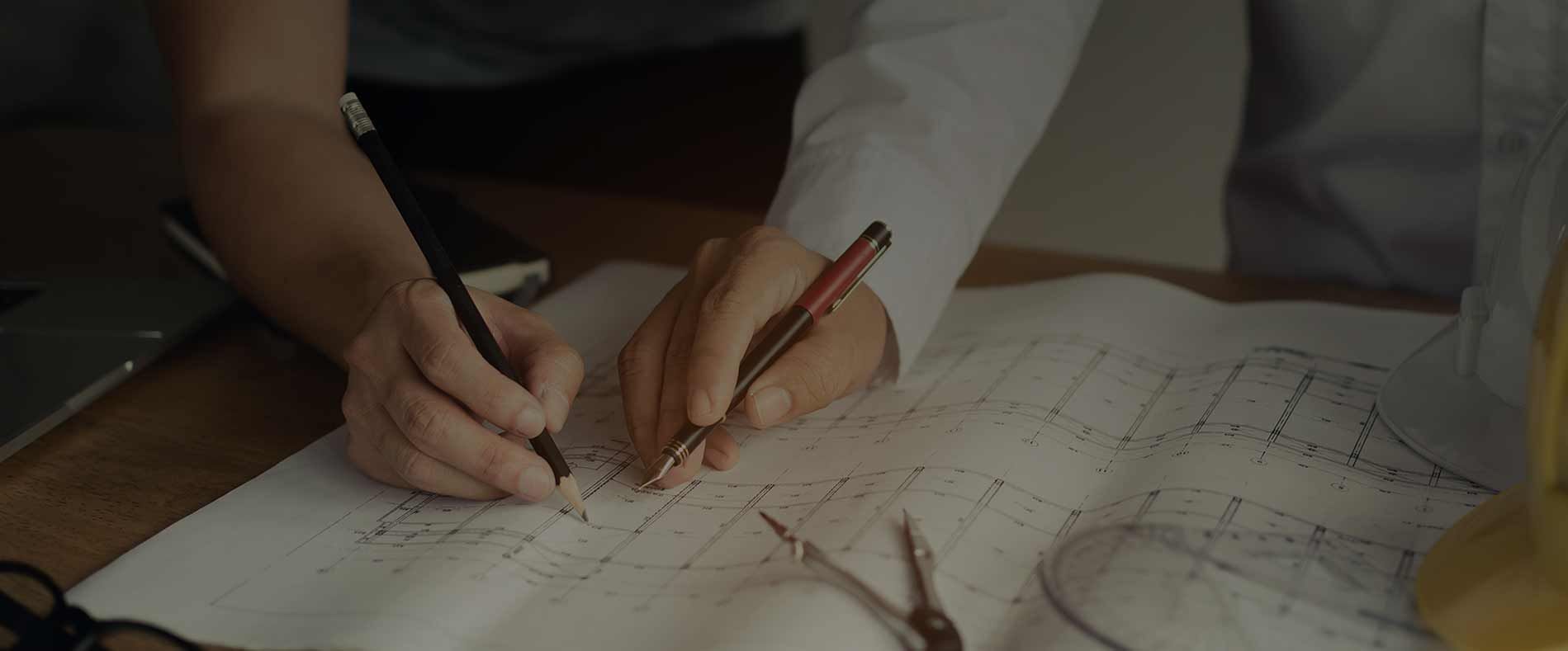 Two hands sketching on paper with pencil and ruler at a desk