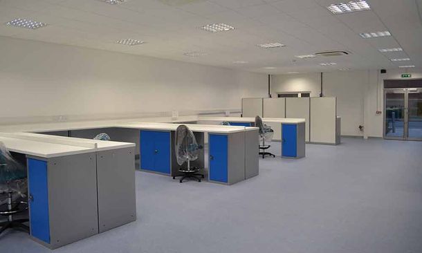 Empty office with blue carpet, white cubicles, and overhead fluorescent lighting