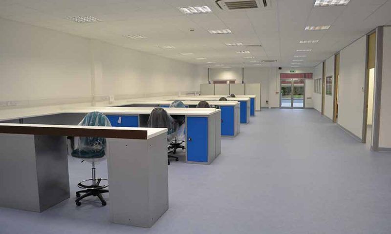 Empty office workspace with rows of desks, blue partitions, and overhead fluorescent lighting
