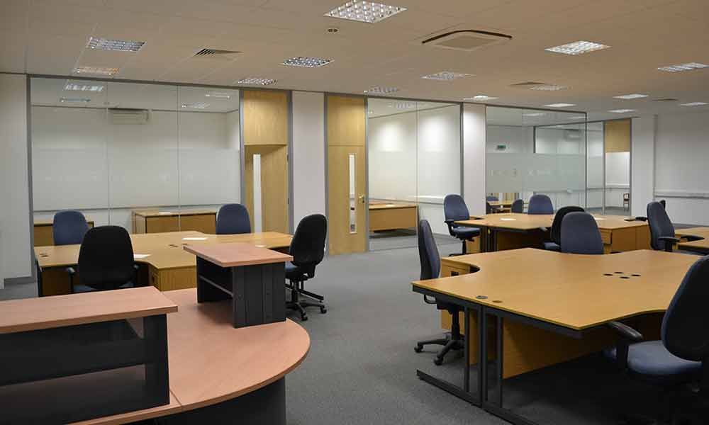 Empty office workspace with desks, chairs, and partitioned workstations under bright ceiling lights