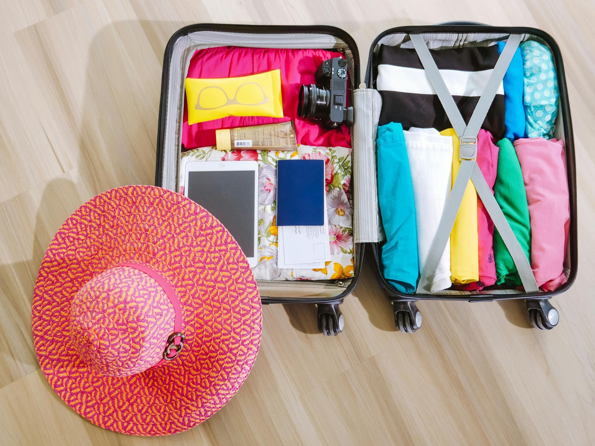Open suitcase packed with clothes, camera, passport, hat, and other travel essentials on wooden floor packing for a Holiday.