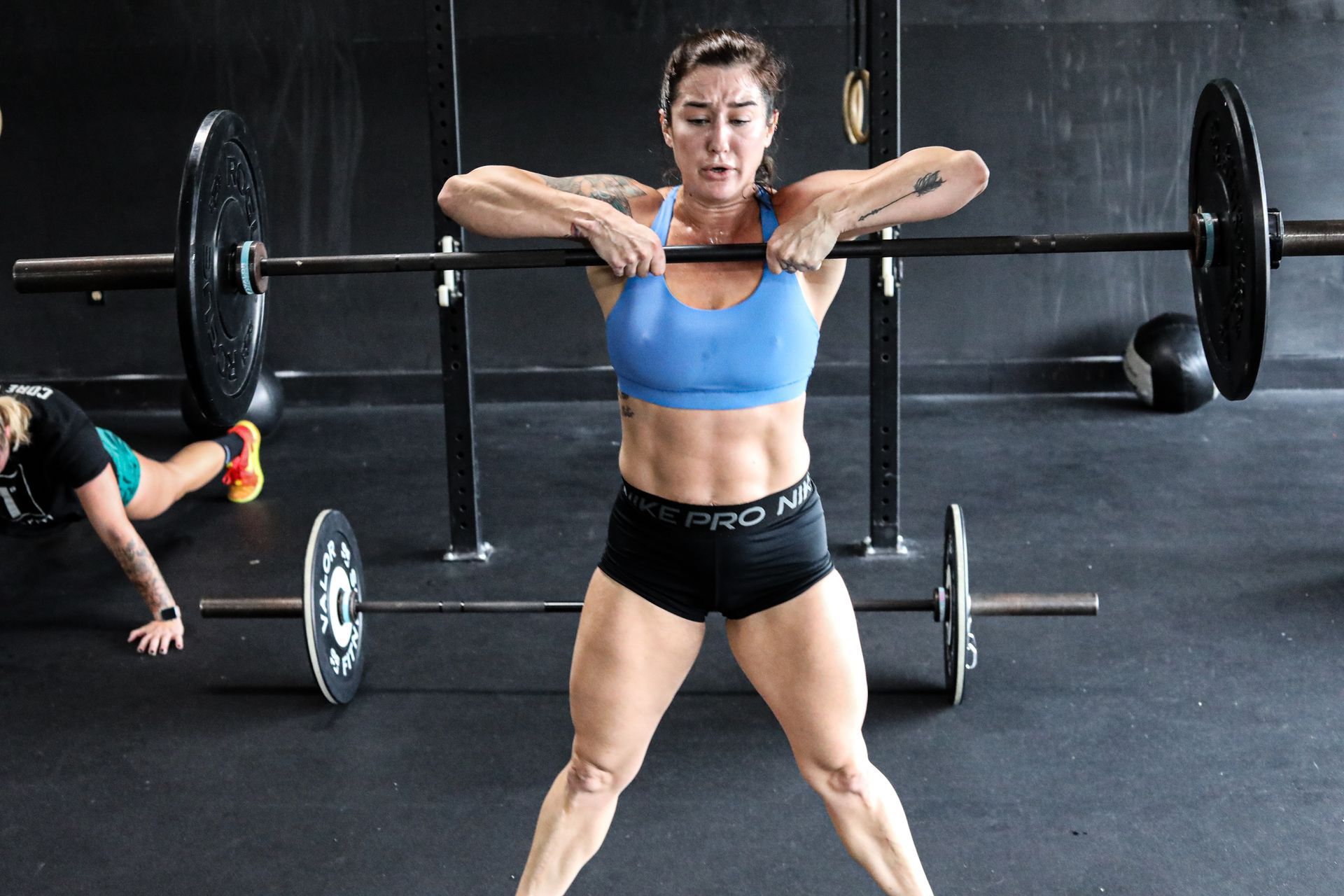 A woman is lifting a barbell over her head in a gym.