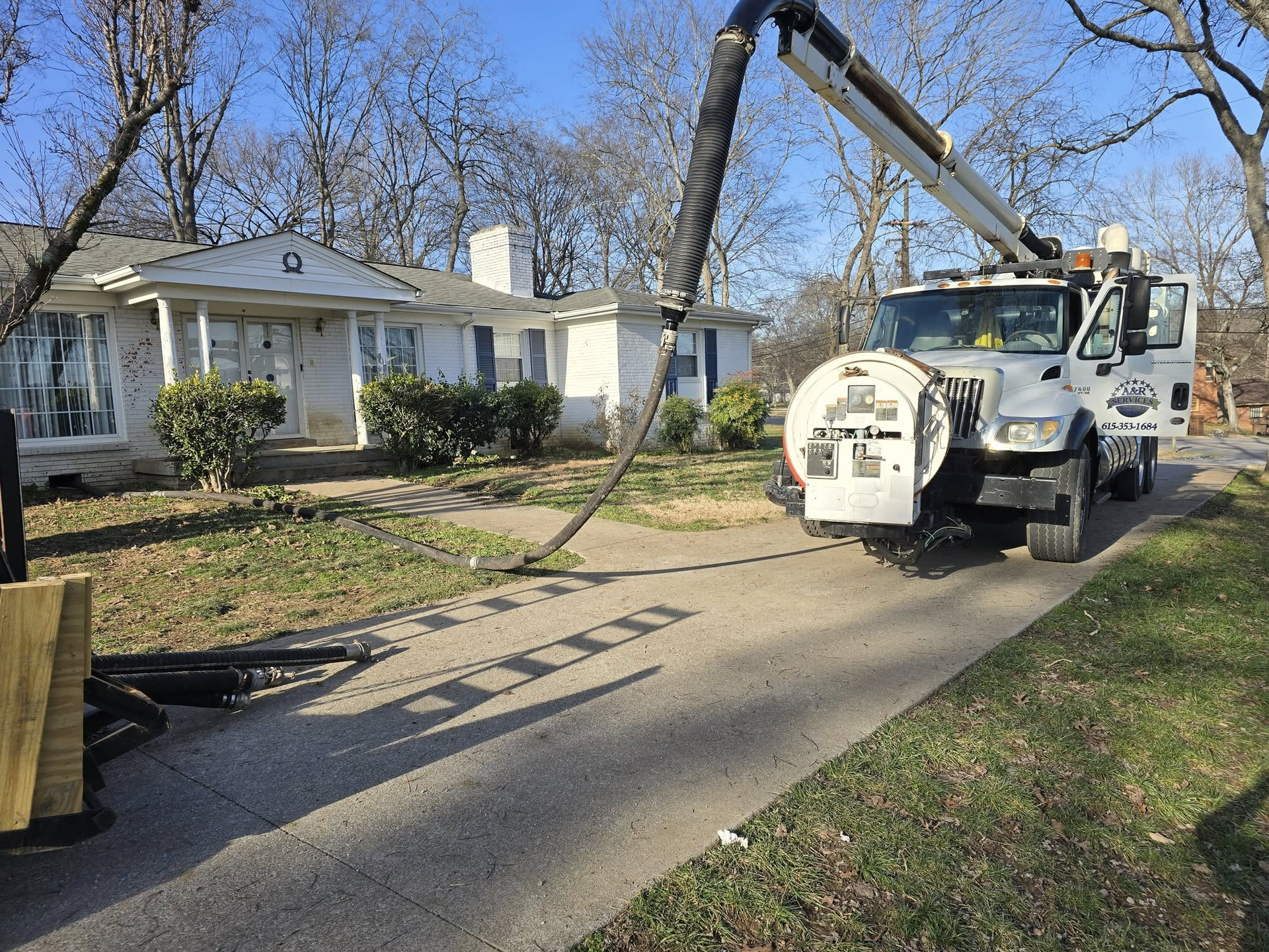 A utility truck with a boom arm uses a vacuum hose to work on an underground project in a residential driveway.