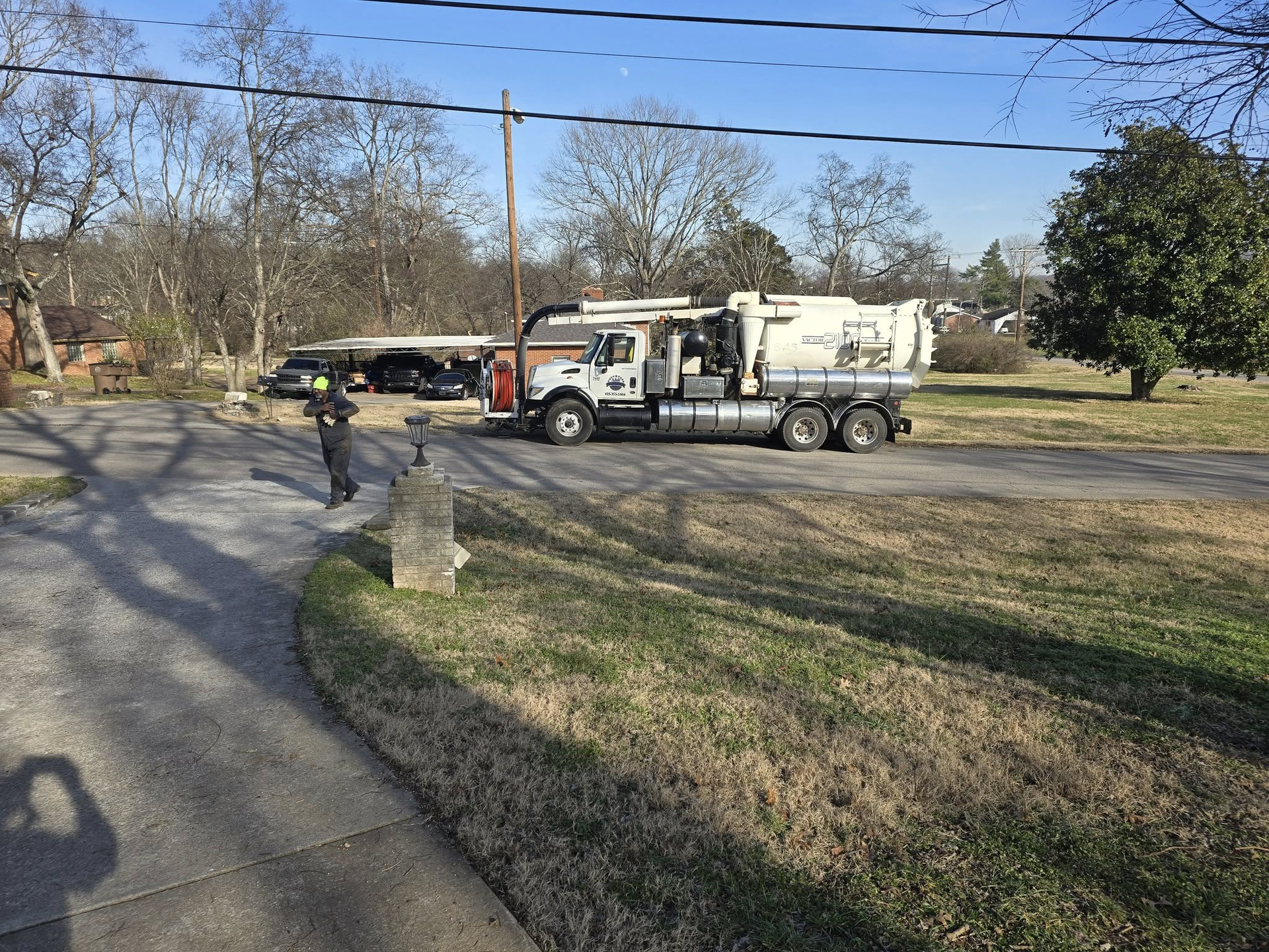 A utility truck parked on a quiet residential street with a worker standing on the sidewalk nearby.