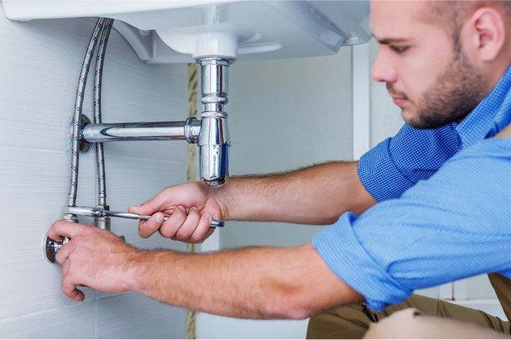 Plumber tightening sink pipes under a bathroom sink with a wrench
