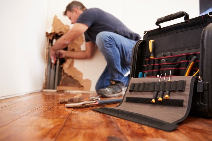 Technician repairing damaged hardwood floor with tools in a black case nearby