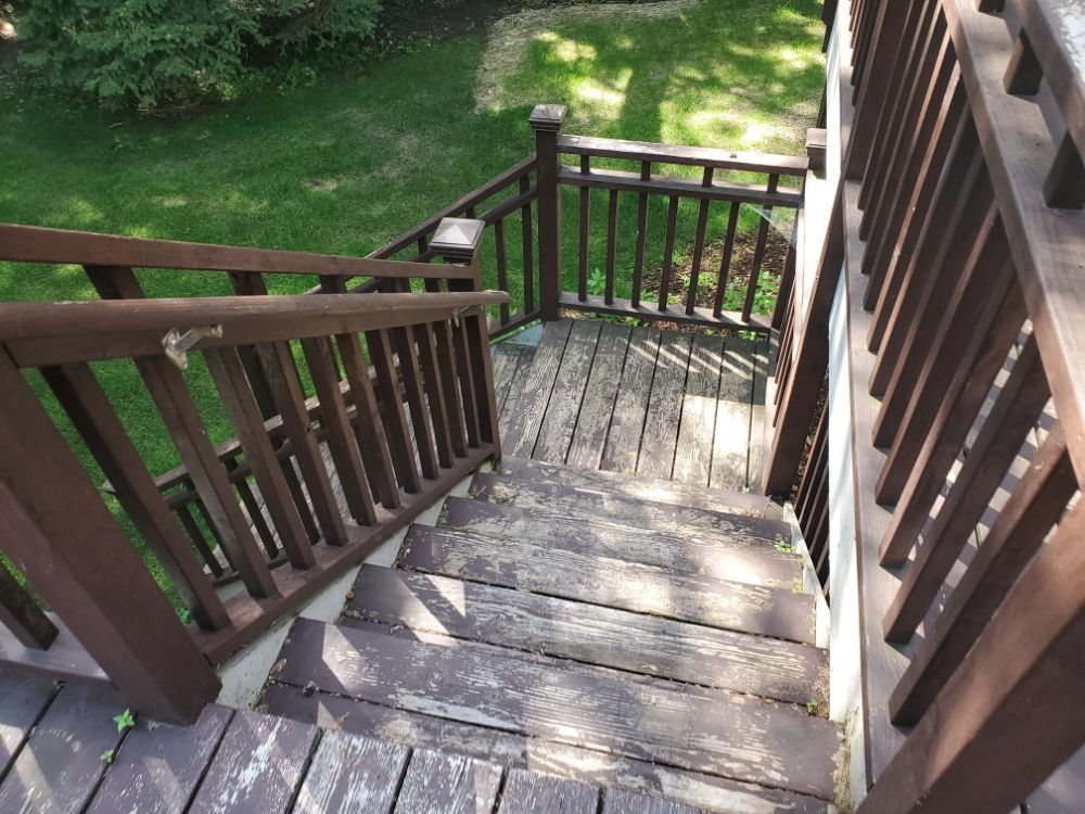 Wooden outdoor stairs leading down from a deck with brown railings.