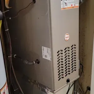 Tall gray HVAC furnace in a narrow utility closet with exposed ductwork and pipes