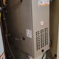 Tall gray HVAC furnace in a narrow utility closet with exposed ductwork and pipes