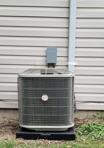 Outdoor air conditioning unit beside a white house wall with gray electrical box above it