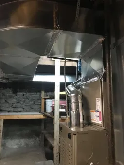 Metal kitchen hood and ductwork above an empty cooking area with stone wall and counter.