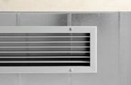 Tall gray HVAC furnace in a narrow utility closet with exposed ductwork and pipes