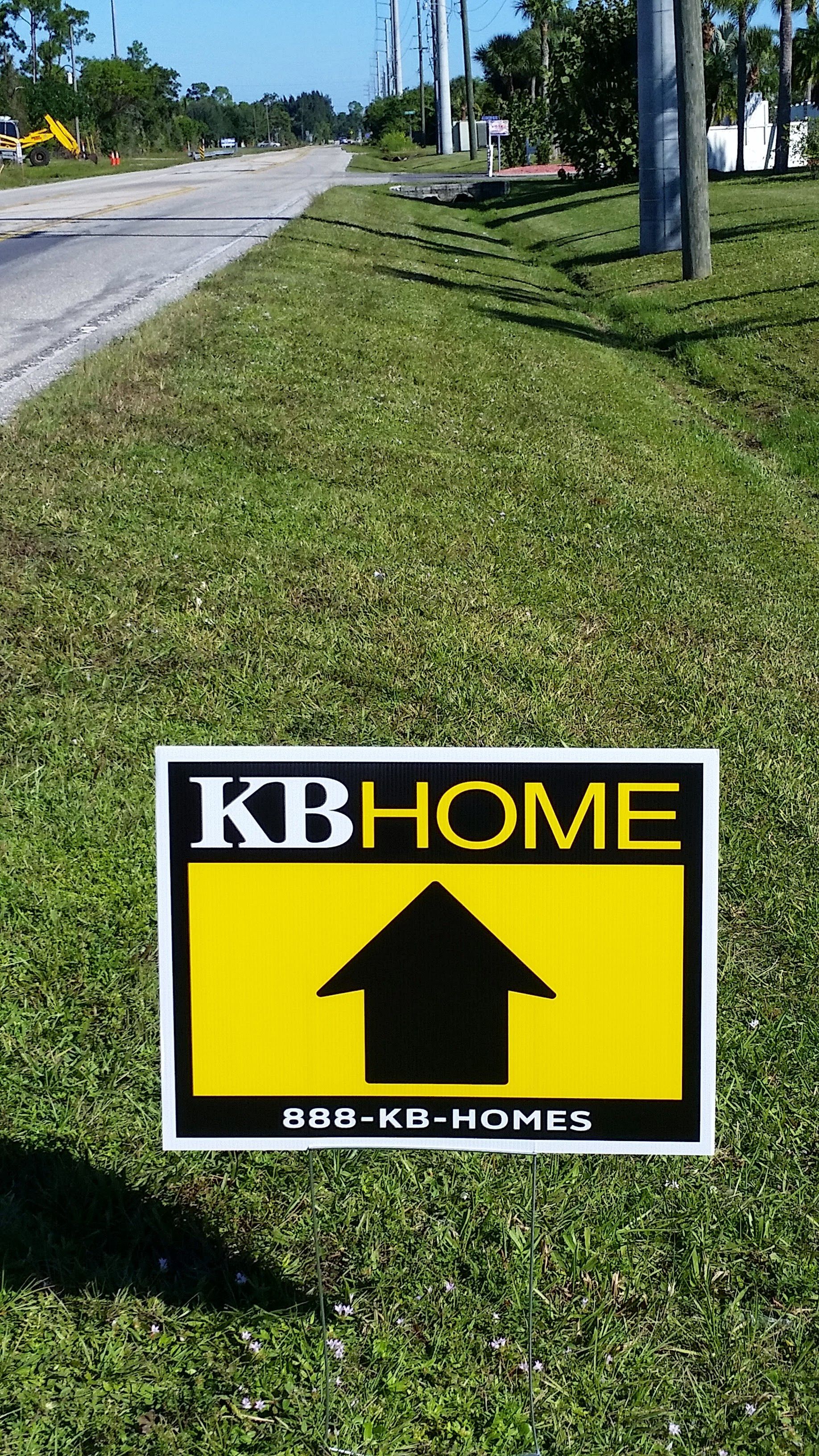 A yellow and black sign with an arrow pointing up is in the grass.