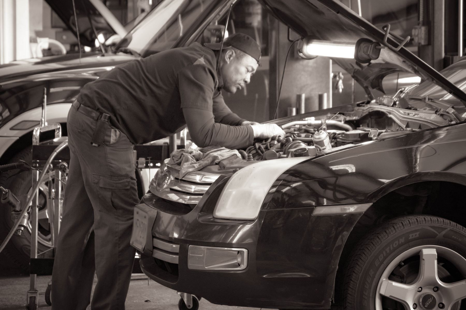 A man is working on the engine of a car in a garage. | C & G Auto Center Inc