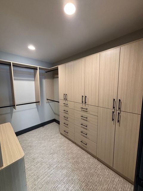 Modern walk-in closet with light wood cabinets, open hanging space, mirrors, and carpeted floor