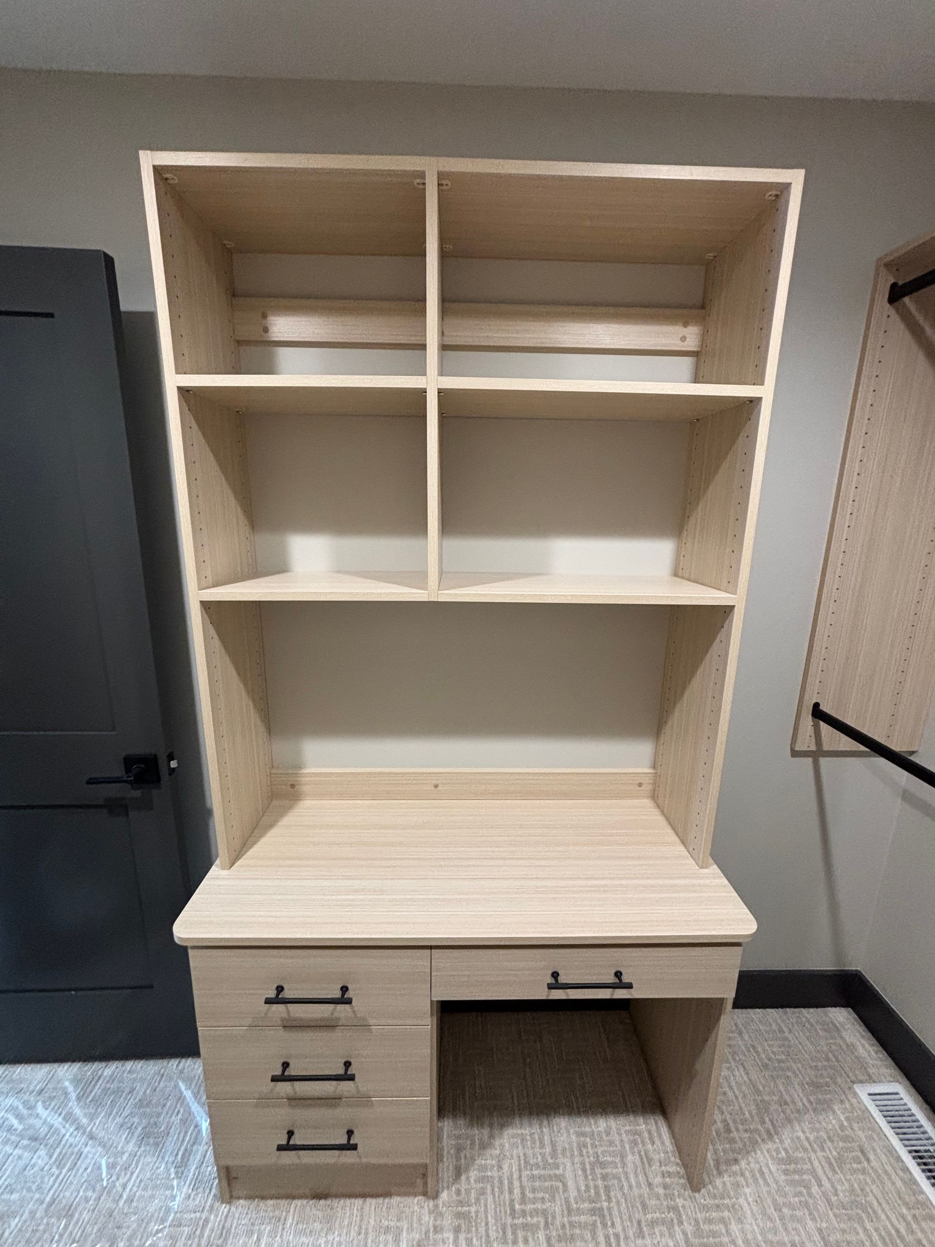 Built-in beige study desk with shelves and drawers against a wall in an empty room