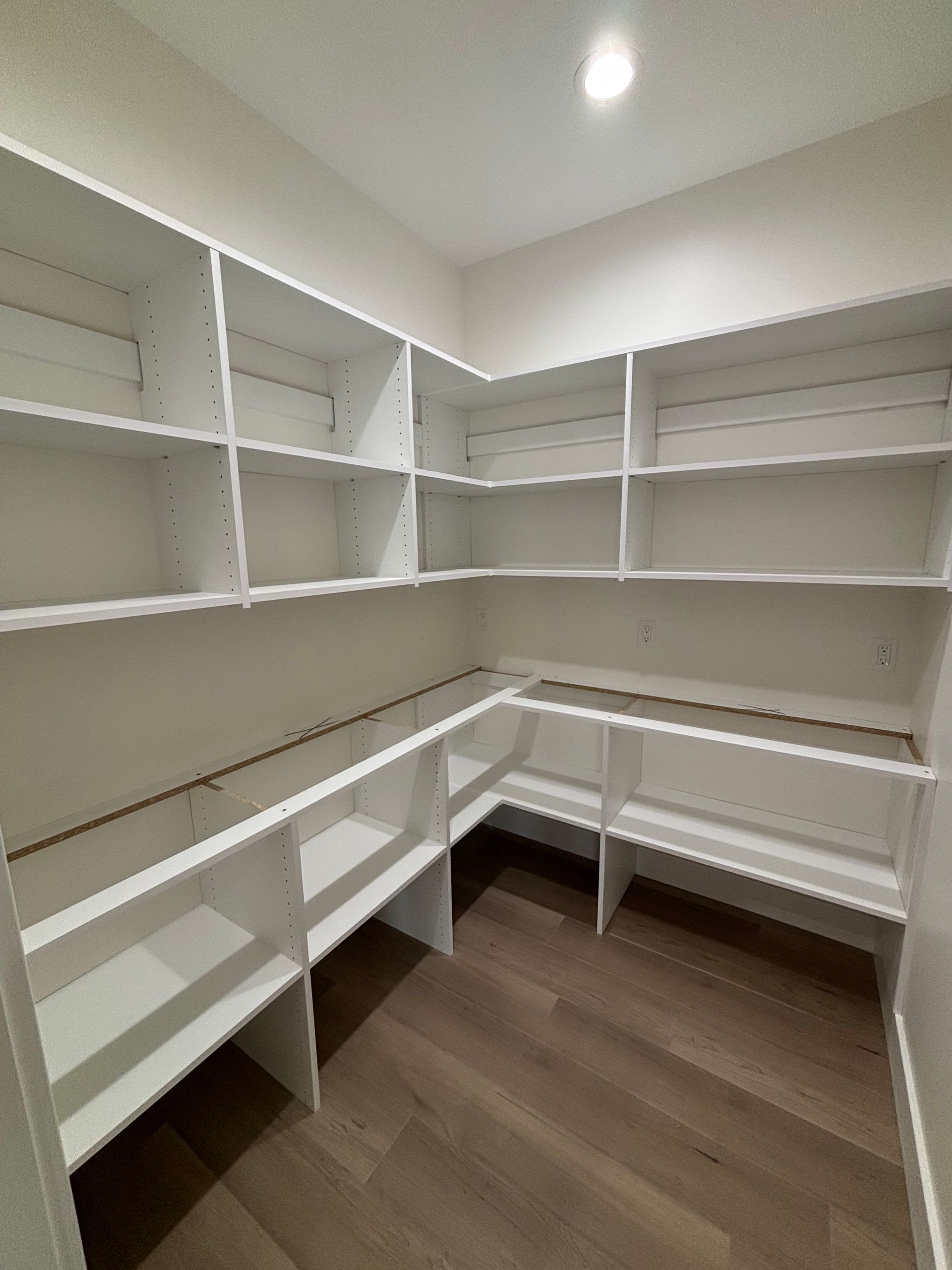 Empty white walk-in closet with wraparound shelves and hanging rods, wood floor, and ceiling light.