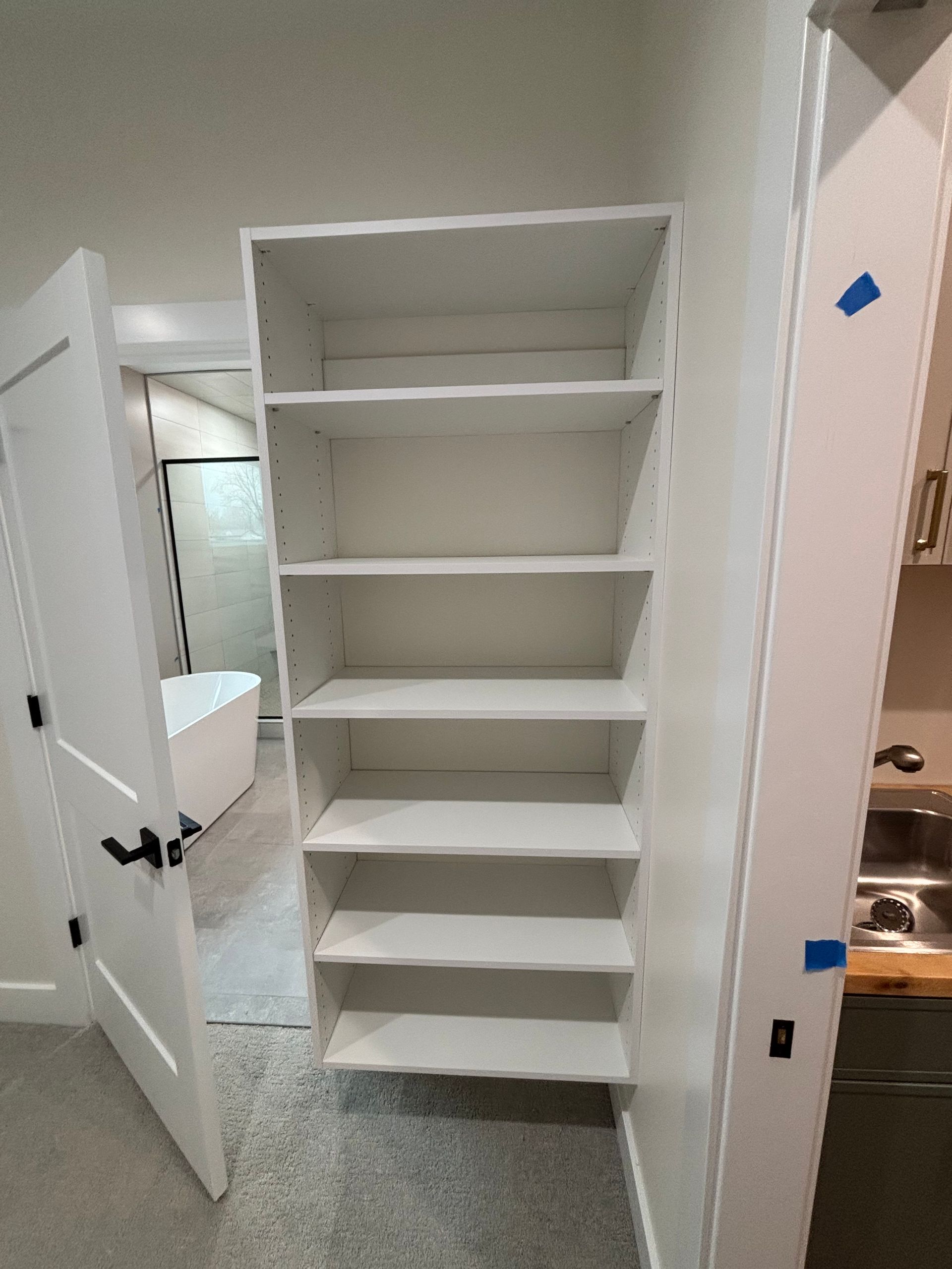 Open white closet shelves in a carpeted room with a bathroom visible to the left.