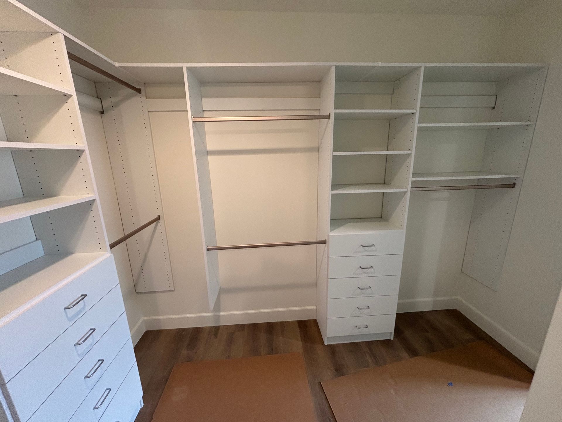 Walk-in closet with white built-in shelves, hanging rods, and drawers on hardwood floors.