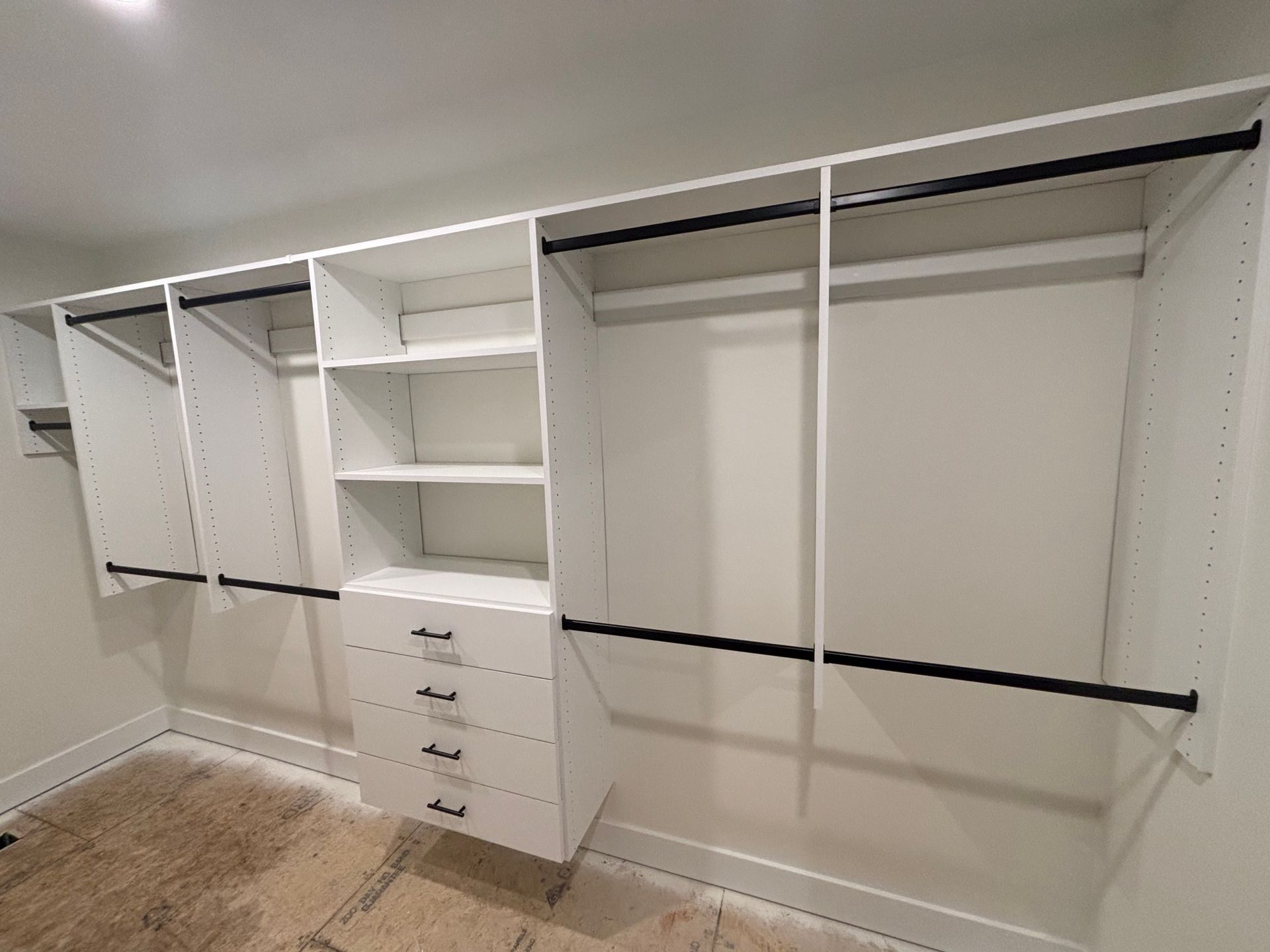 White walk-in closet with open shelving, drawers, and hanging rods, viewed from the doorway.