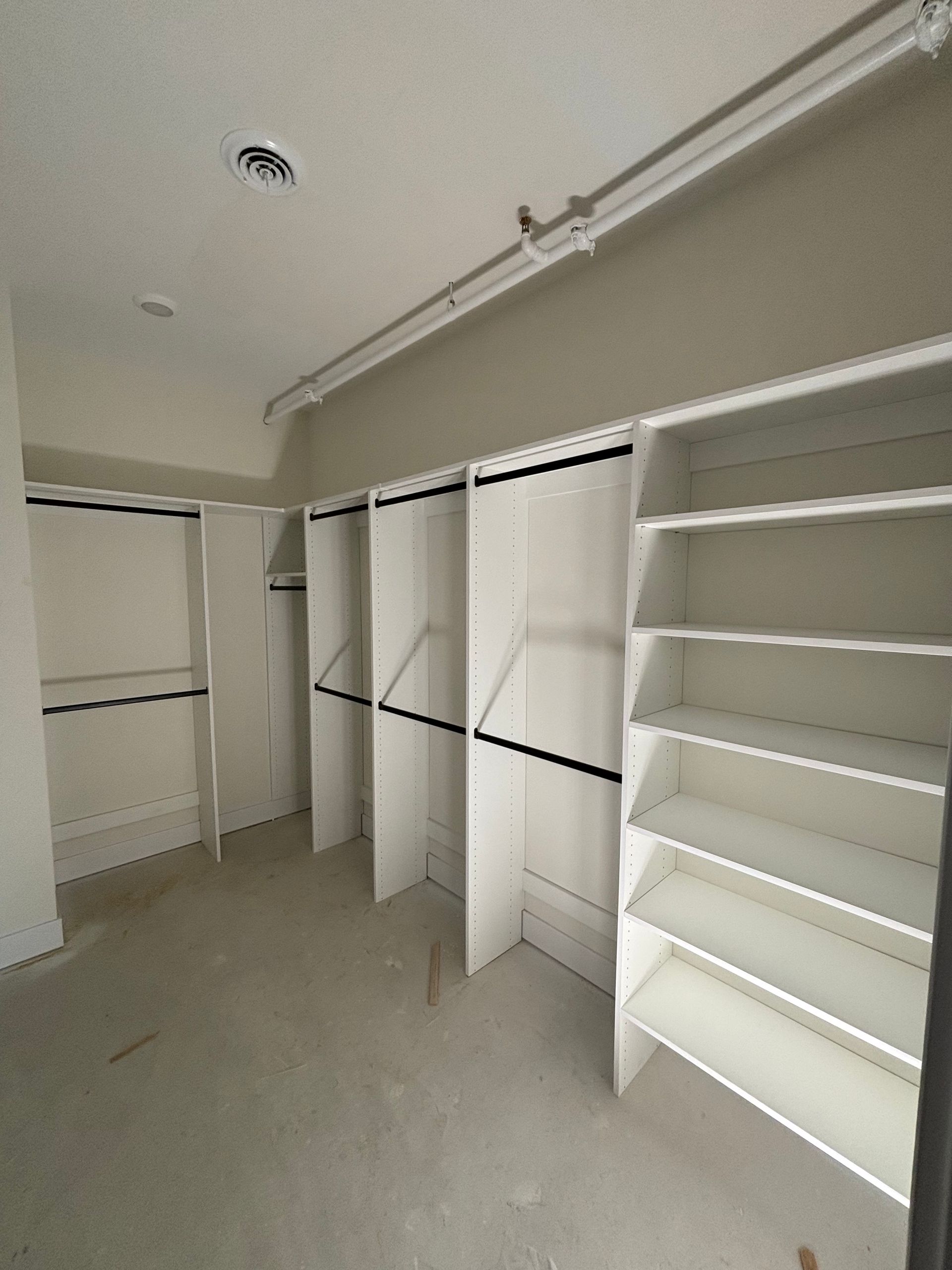 Empty walk-in closet with white shelves, hanging rods, and beige carpet.