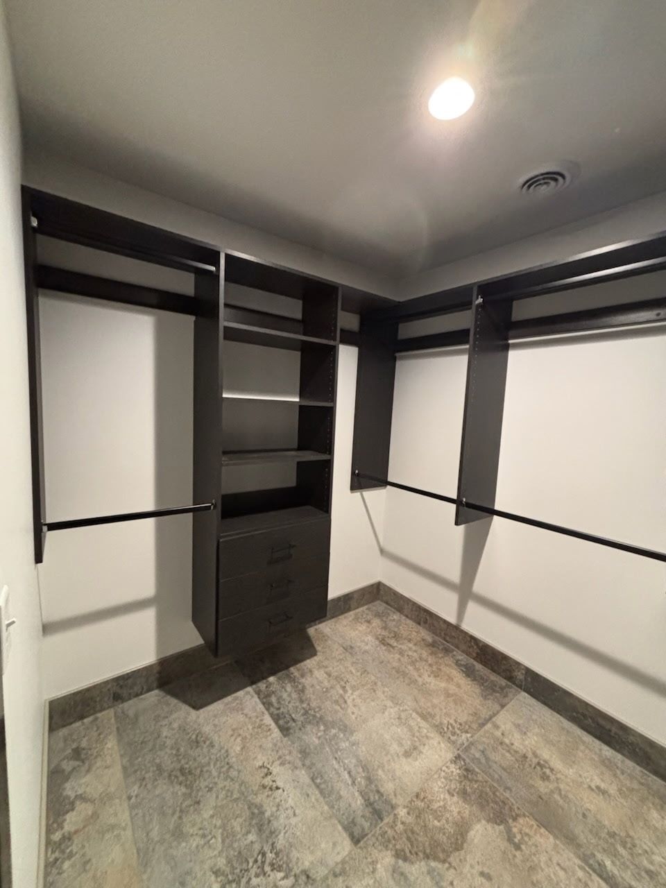 Walk-in closet with white walls, black shelving, drawers, and a patterned tile floor