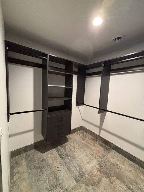 Empty walk-in closet with black shelving, white walls, and gray patterned flooring.