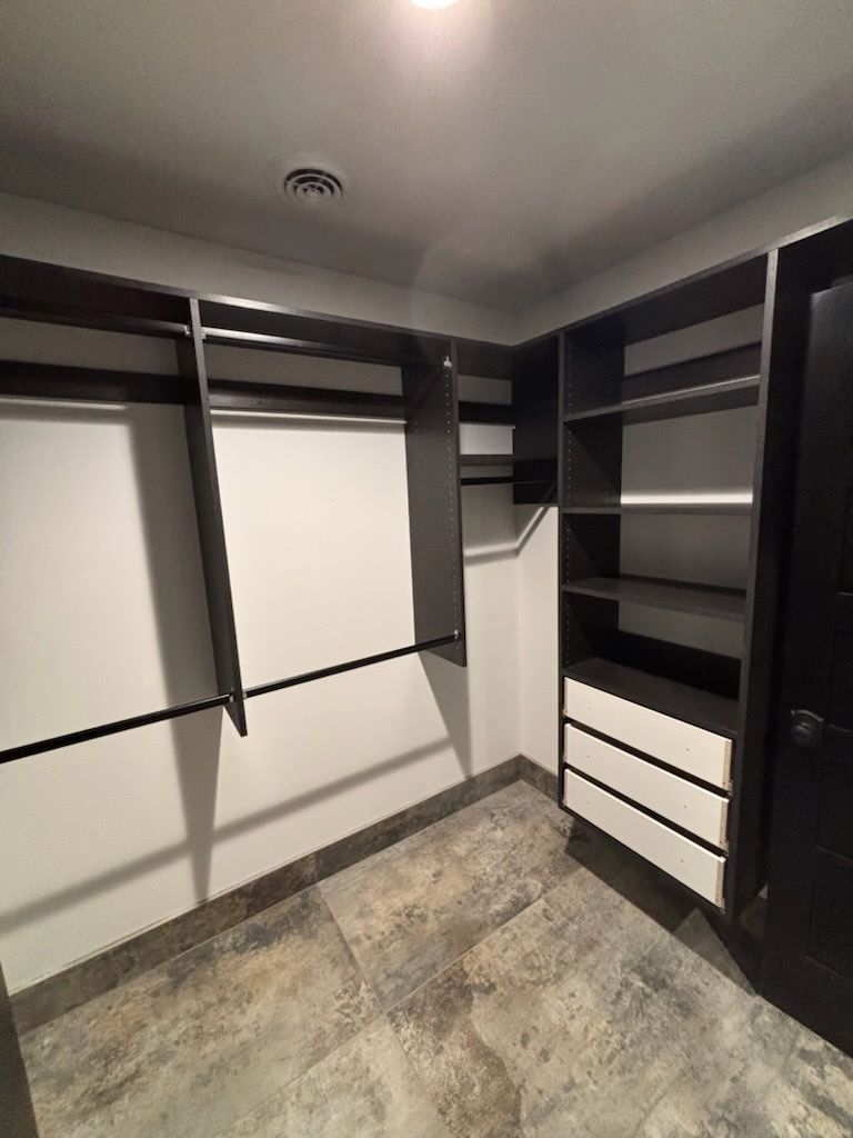 Empty walk-in closet with dark shelves, hanging rods, and gray flooring.
