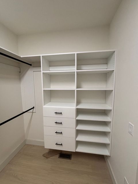 White walk-in closet with shelves, drawers, hanging rods, and beige carpet.