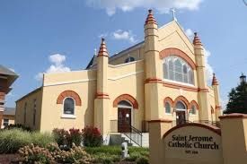 St. Jerome Catholic Church, yellow building with red trim, under blue sky with a sign.