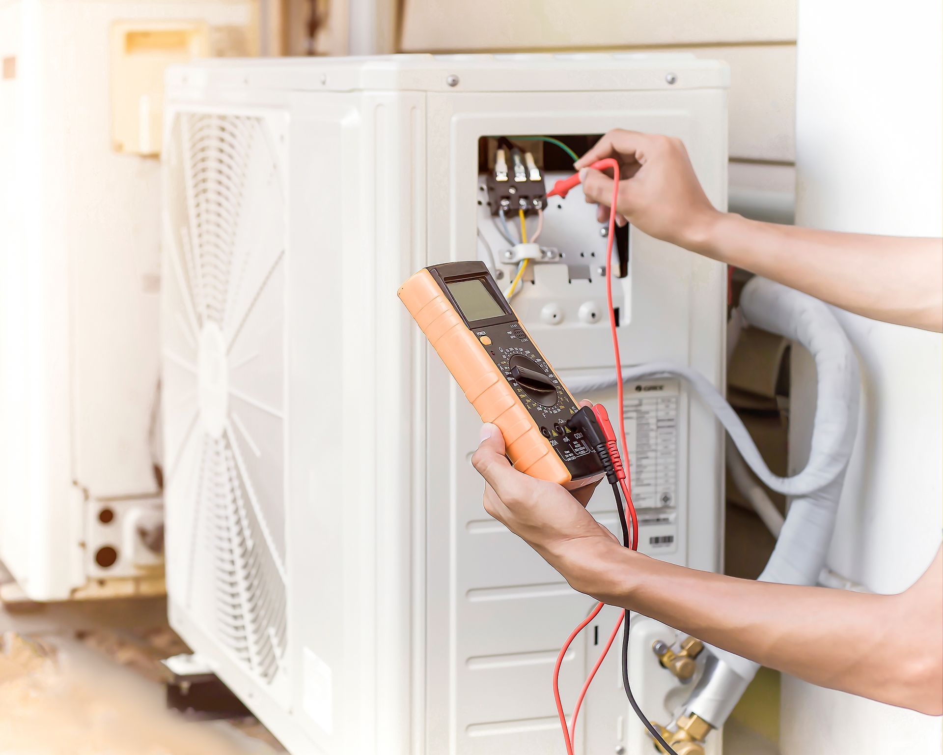 Technician using a multimeter to test the electrical connections on the side panel of an outdoor air conditioning unit.