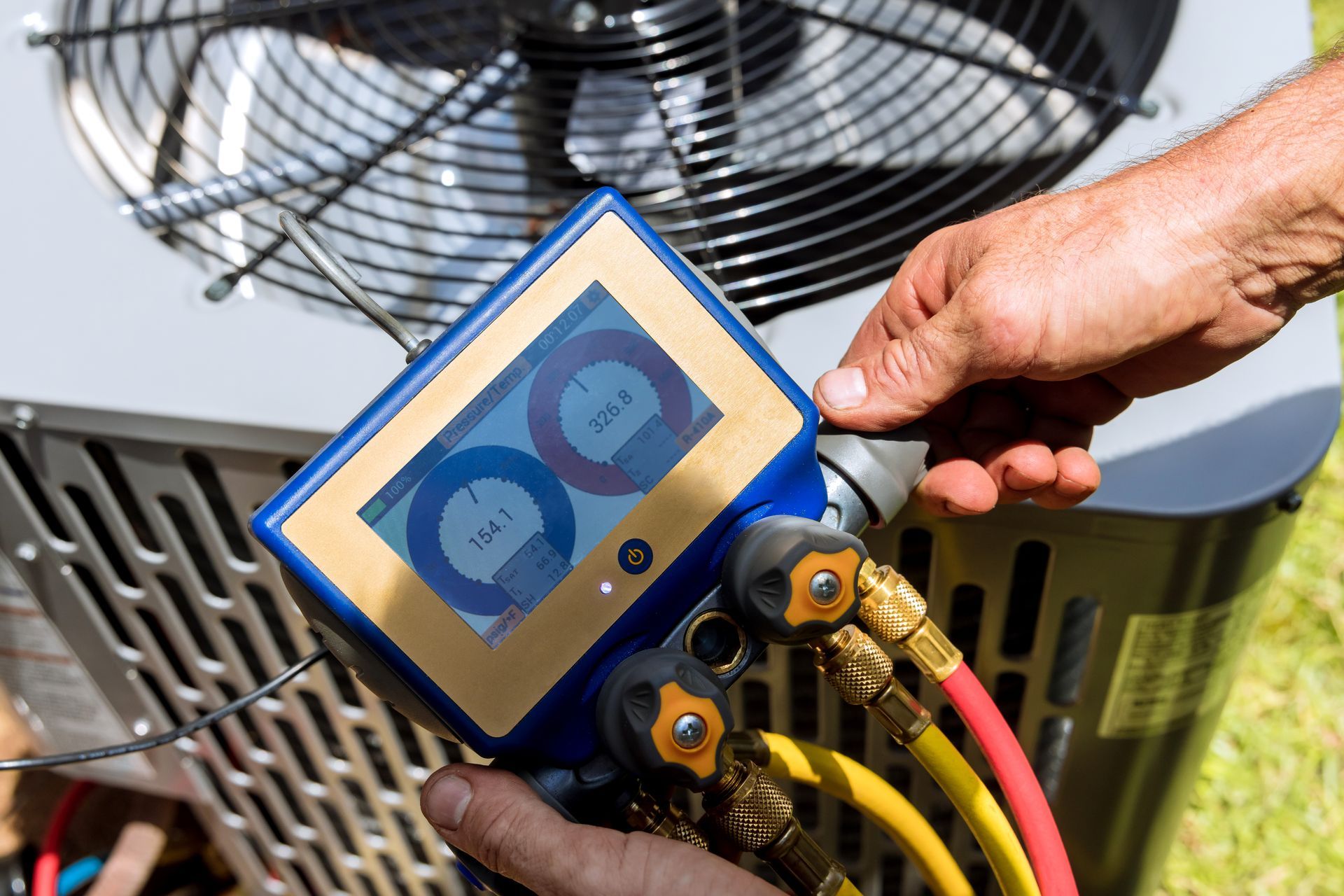 A technician using a digital manifold gauge to check pressure readings on an outdoor HVAC unit.