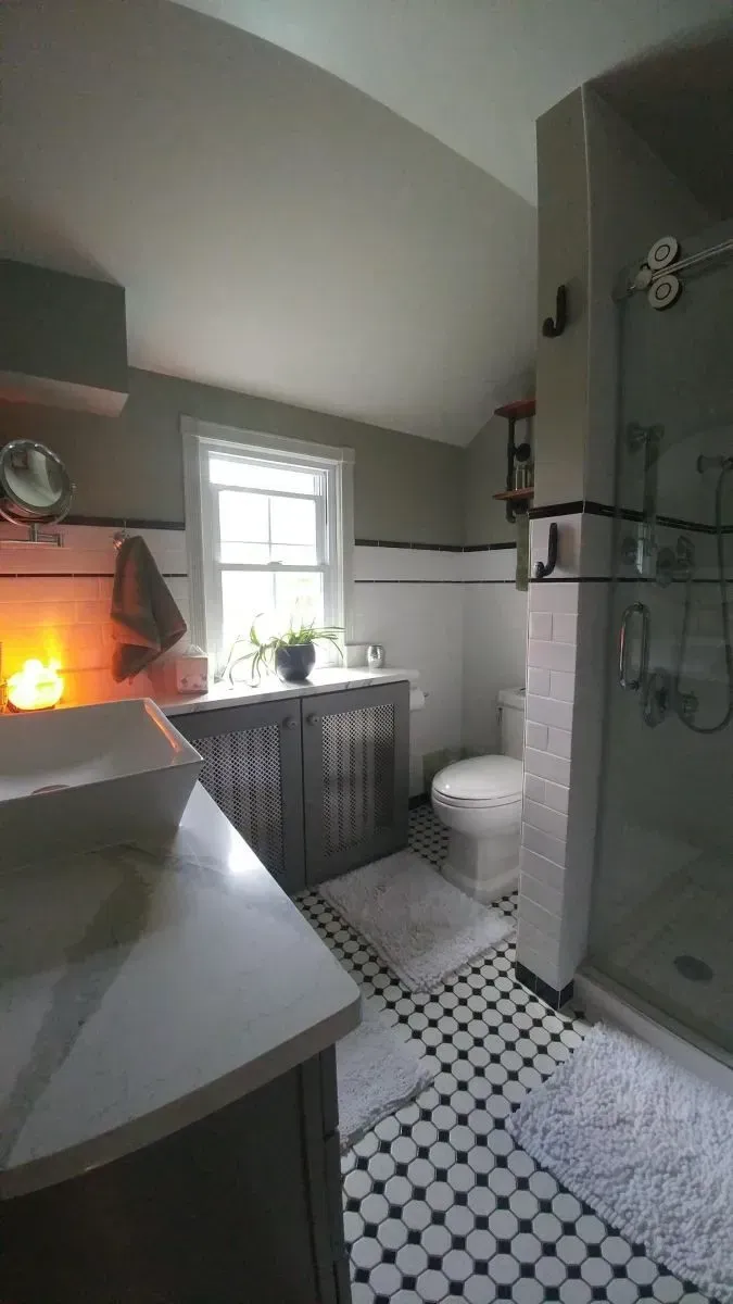 A bathroom with a sink , toilet , shower and window.