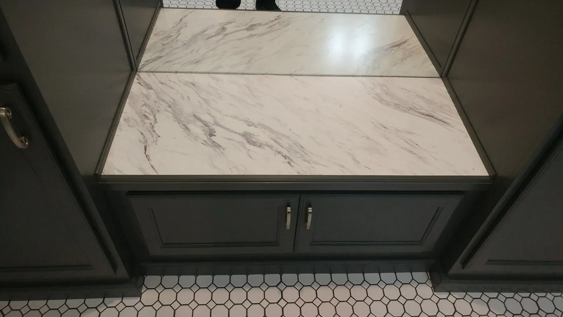 A bathroom with a marble counter top and black cabinets.