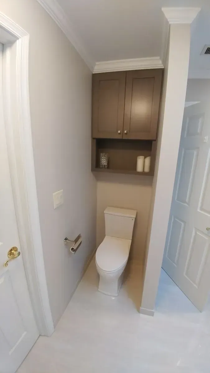 A bathroom with a toilet , cabinets and a door.