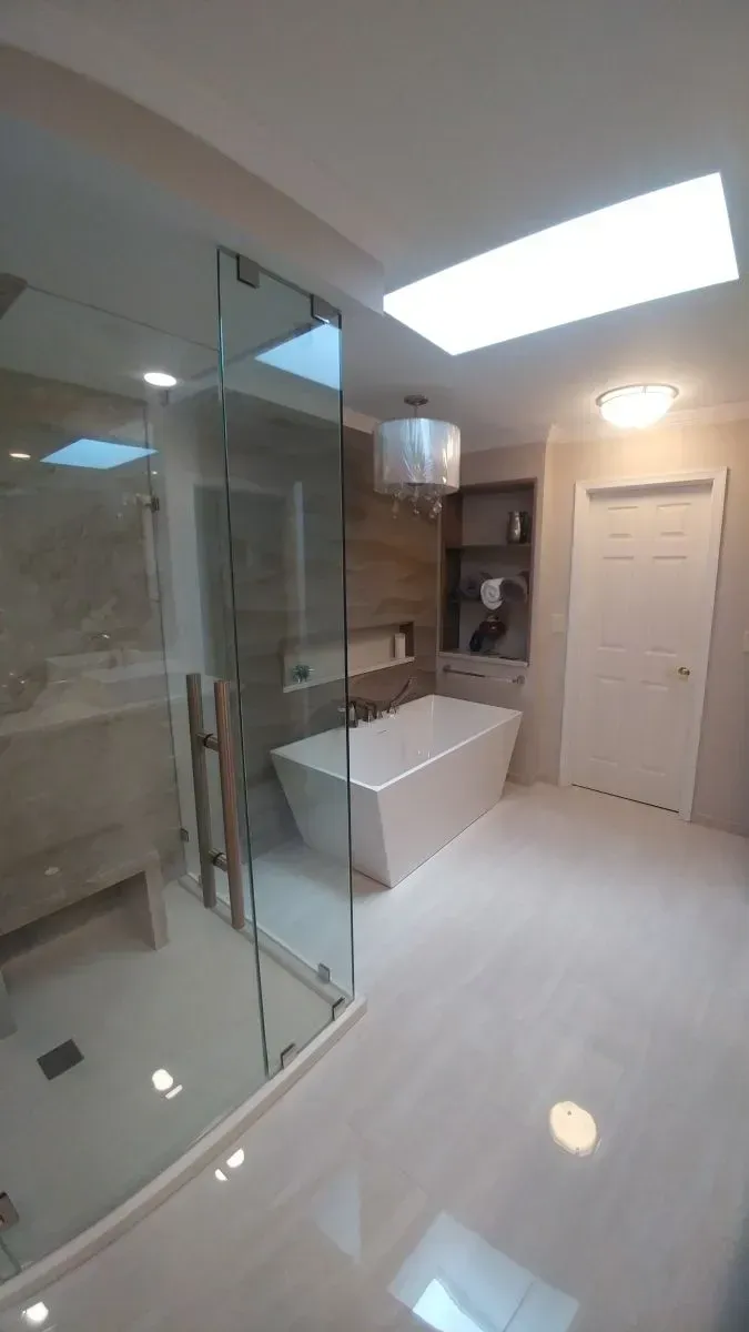 A bathroom with a tub , sink , shower and skylight.