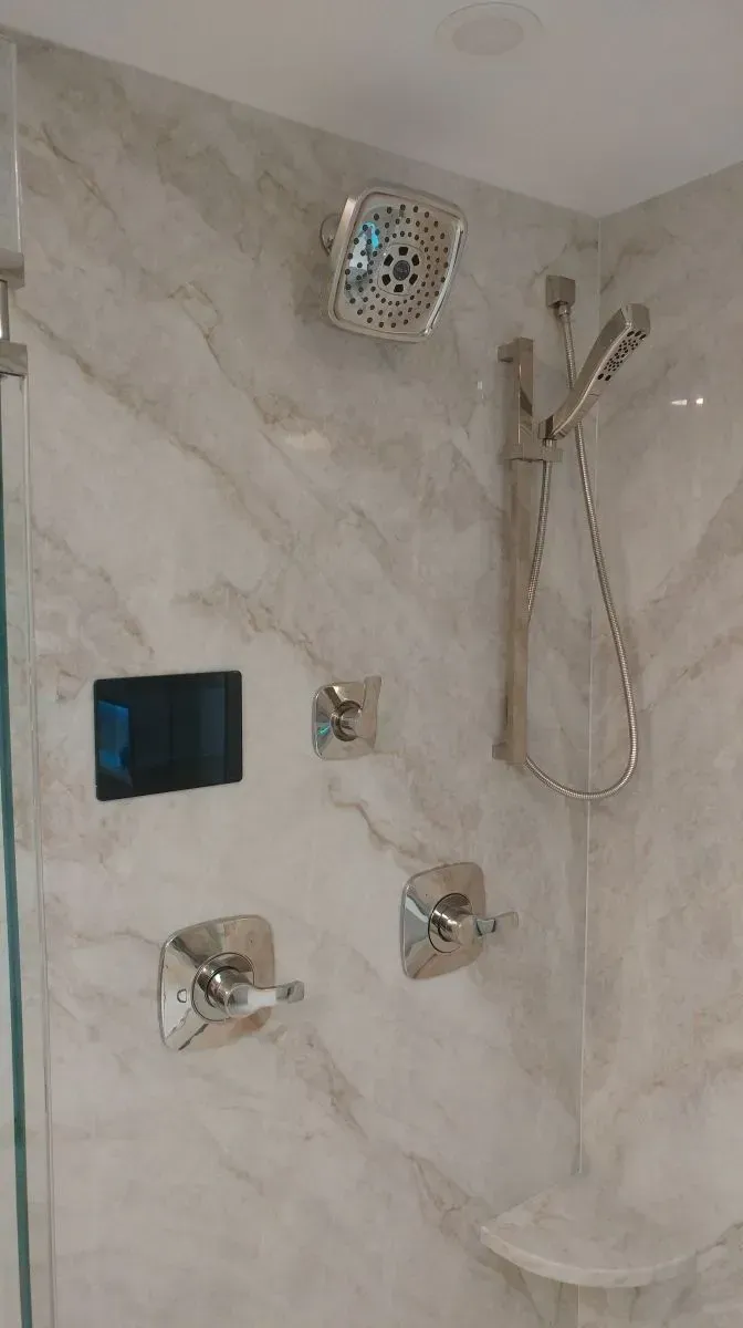 A bathroom with a shower and a television on the wall.