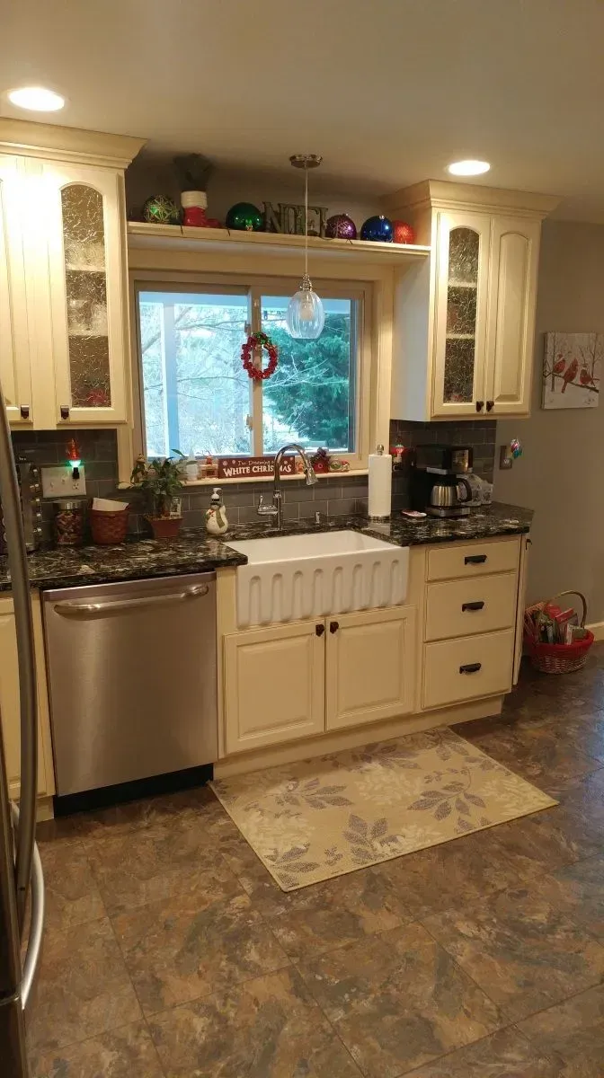A kitchen with white cabinets , stainless steel appliances , a sink and a window.