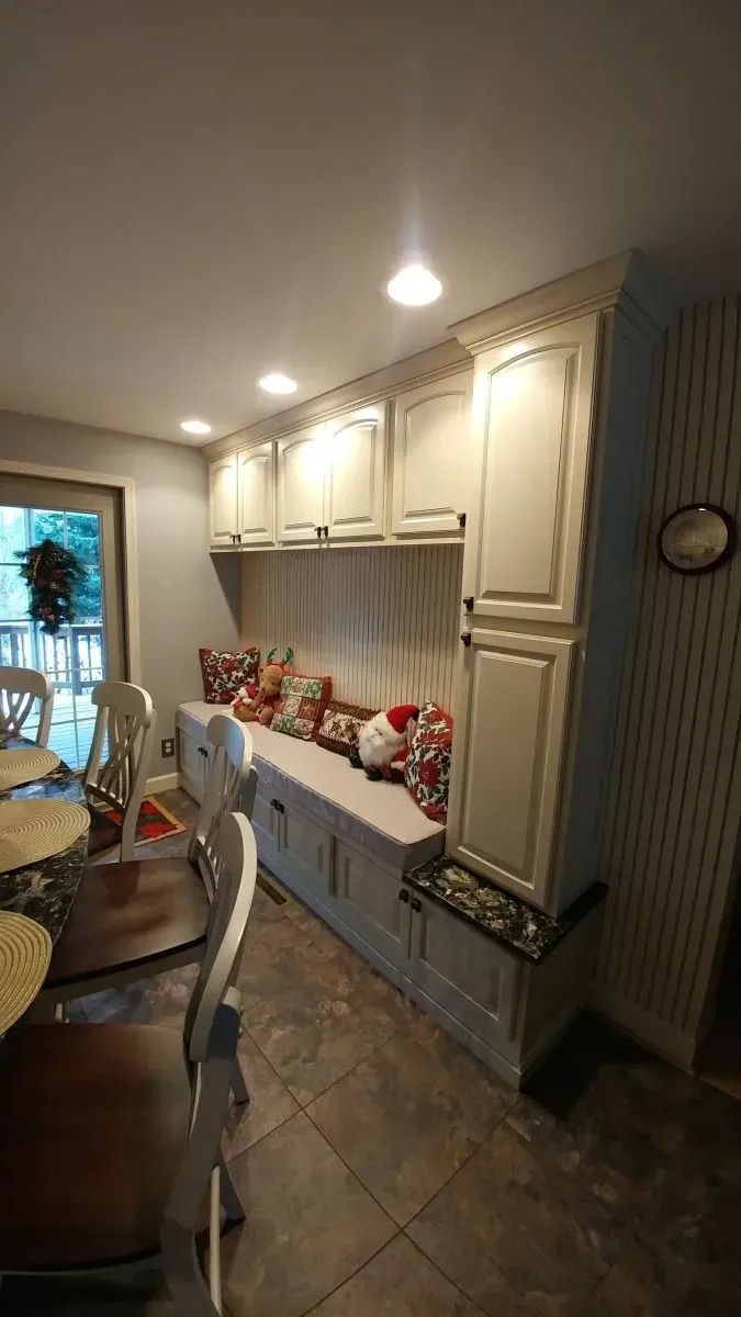 A kitchen with white cabinets , a bench , a table and chairs.