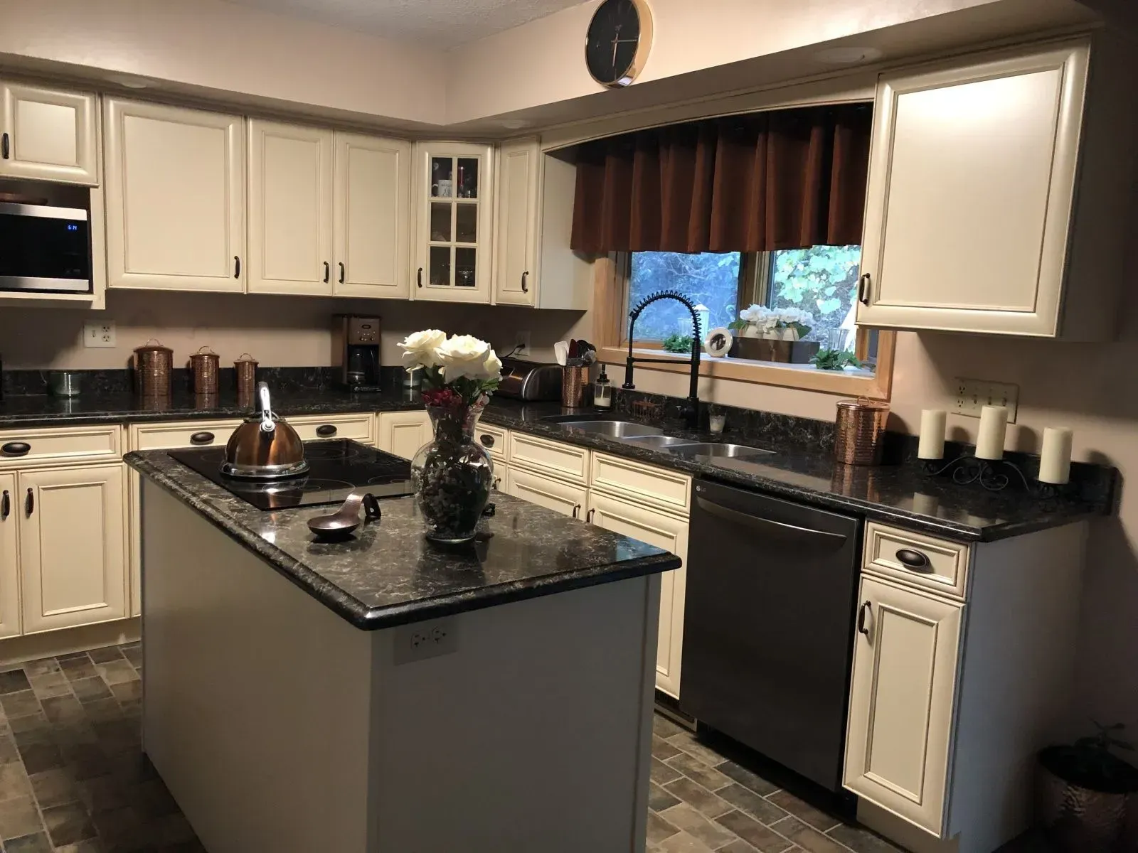 A kitchen with white cabinets , black counter tops , and a large island.