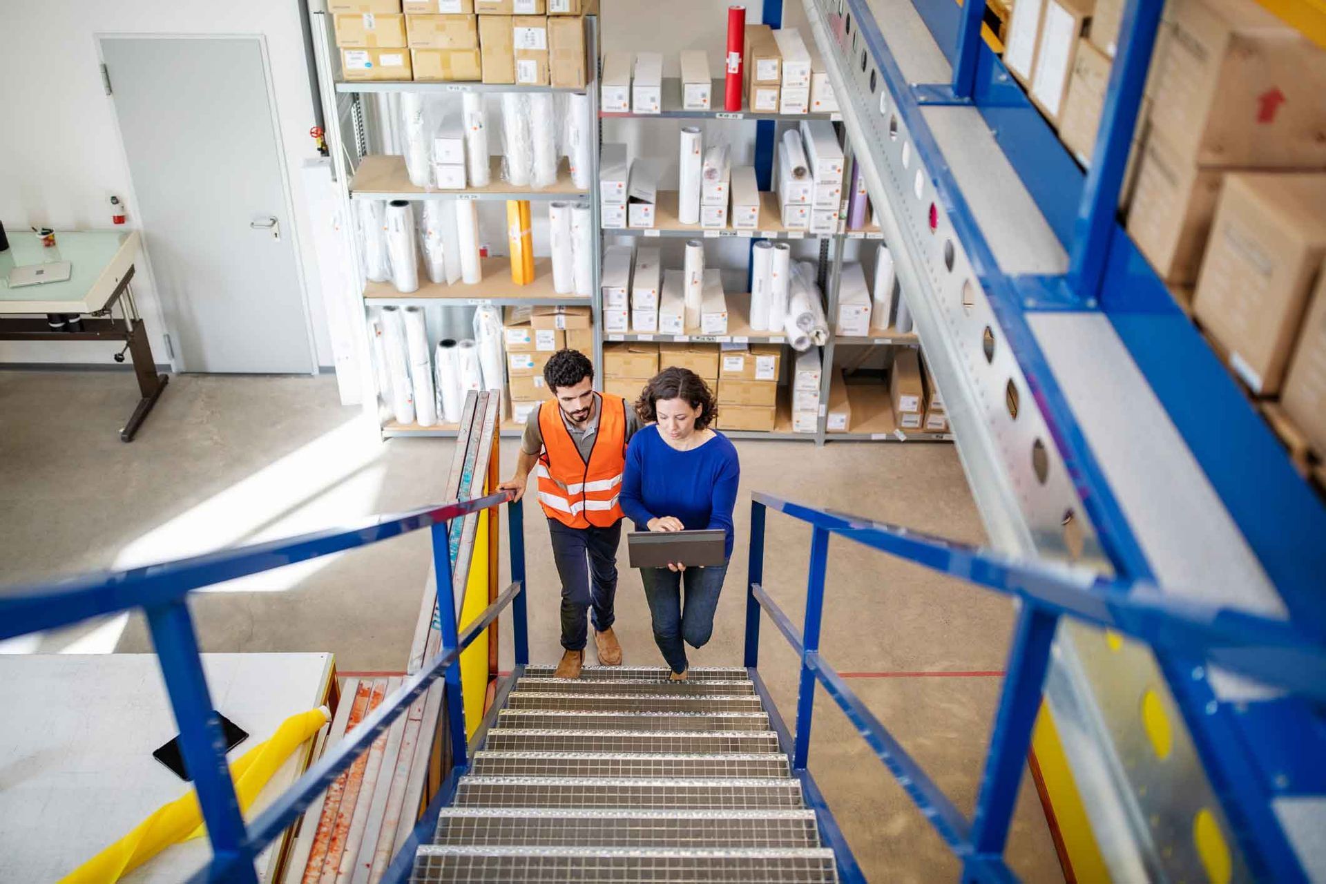 A man and a woman are walking up stairs in a warehouse.