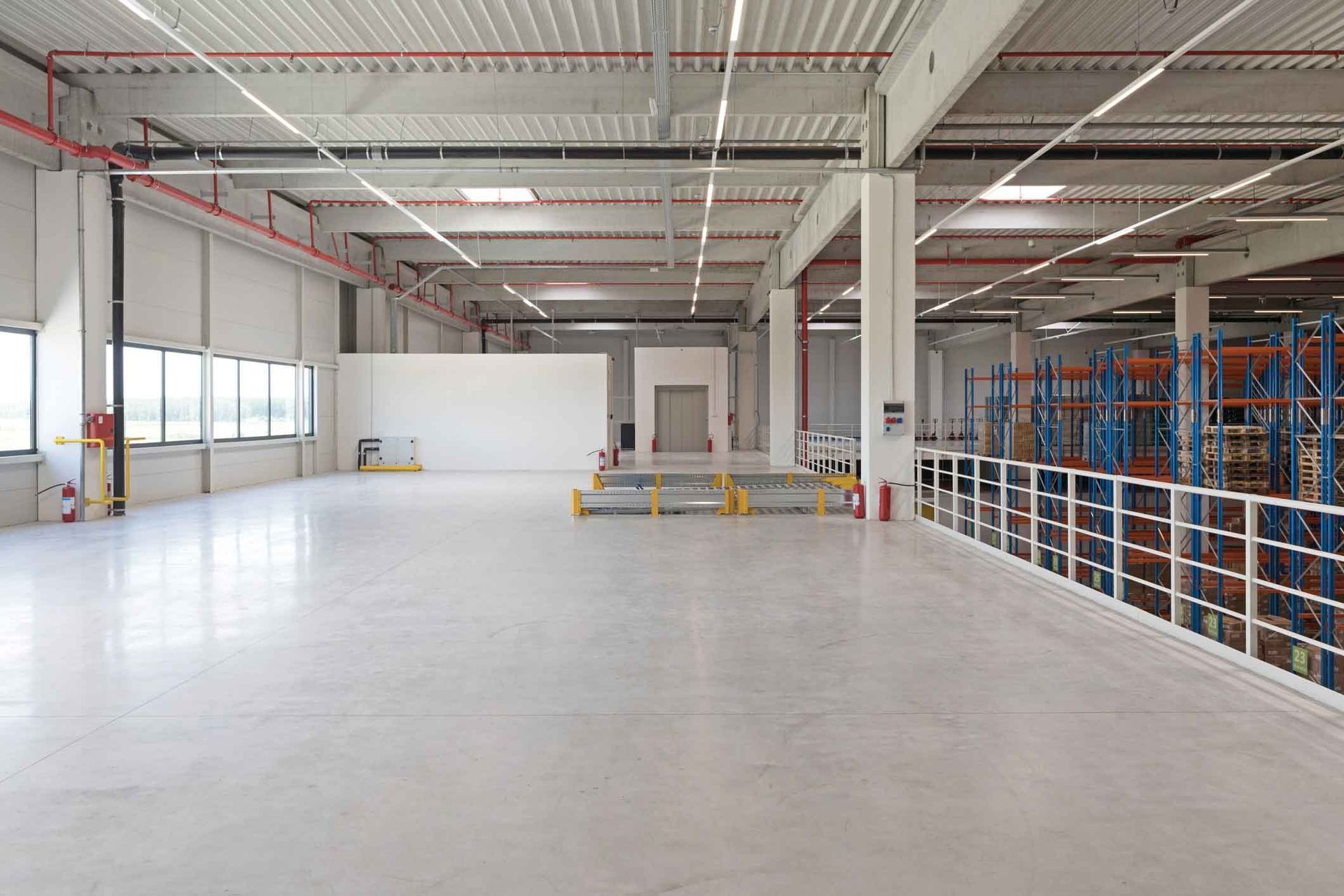A large empty warehouse with lots of shelves and windows.