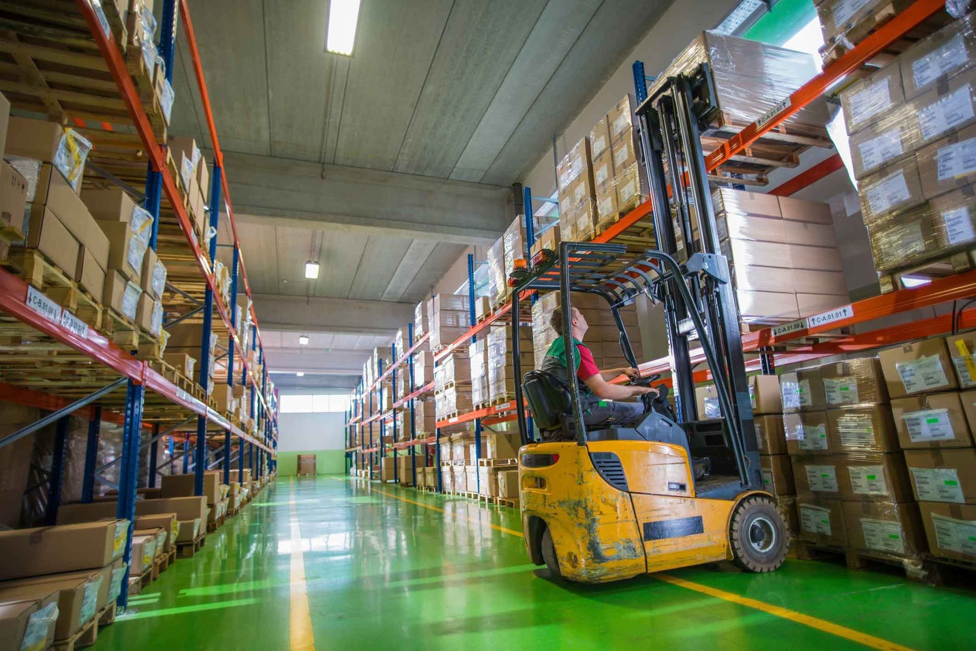 A man is driving a forklift in a warehouse filled with lots of boxes.