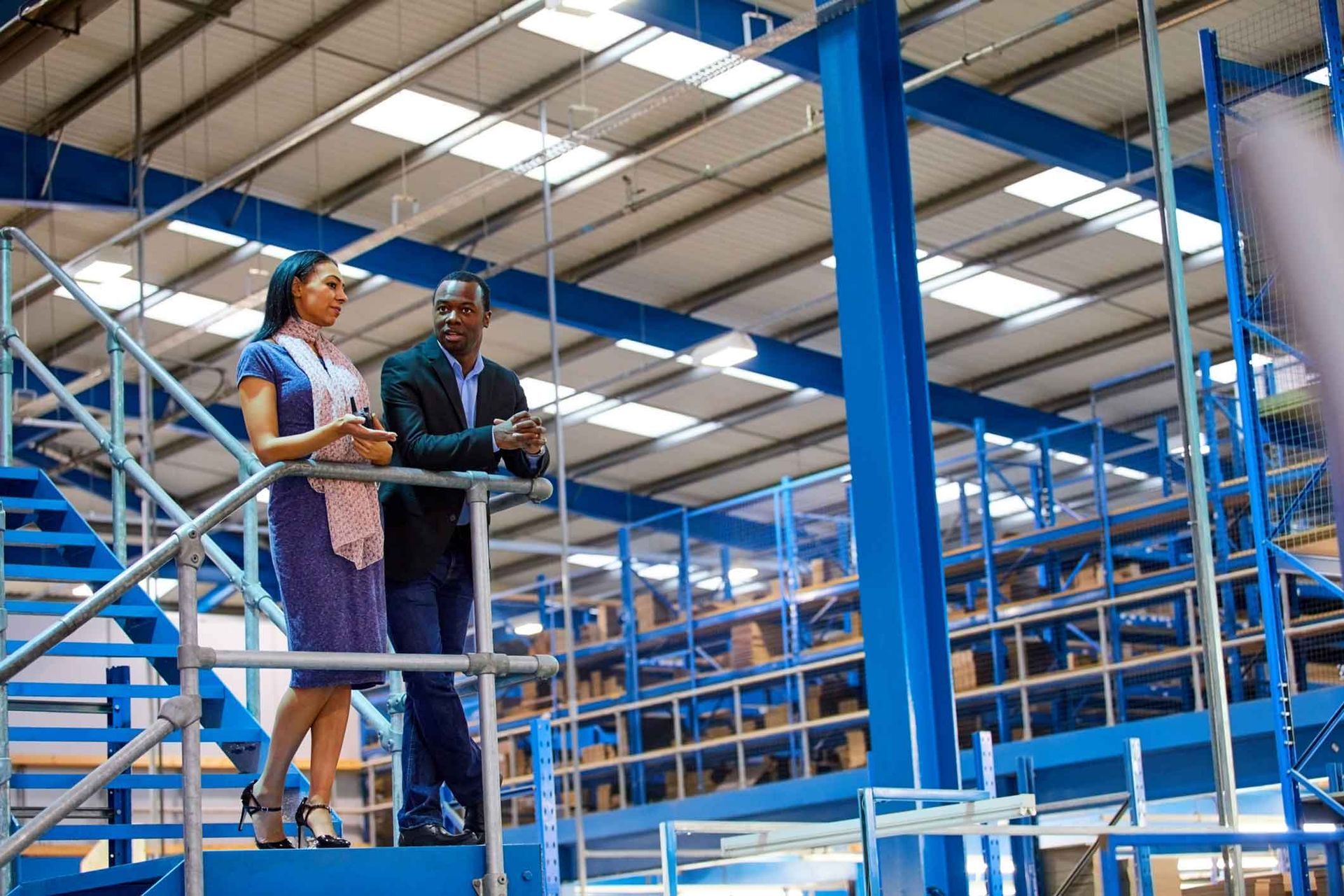 A man and a woman are standing on stairs in a warehouse.