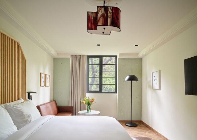 Habitación de hotel con cama, sofá, ventana y pantalla de lámpara con un estampado único.
