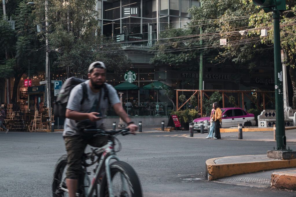 Un hombre en una bicicleta de ruedas gruesas cruza una esquina con un Starbucks detrás de él.