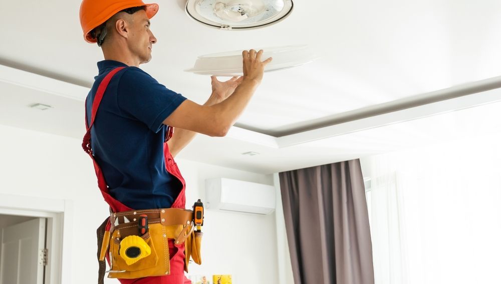 A man is fixing a light fixture on the ceiling in a living room.